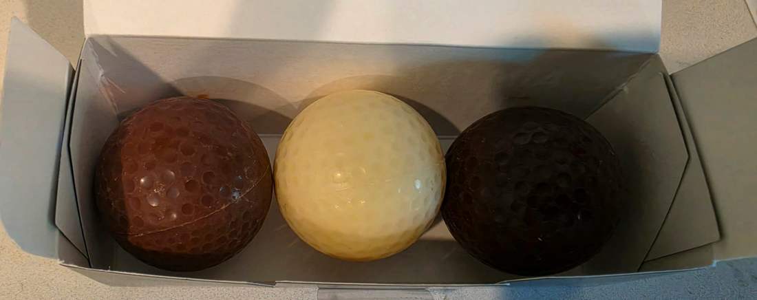 Milk, white, and dark chocolate golf balls in an open presentation box