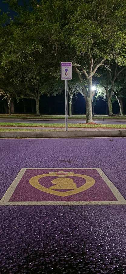 Purple Heart emblem painted beside a reserved Combat Wounded parking sign at night