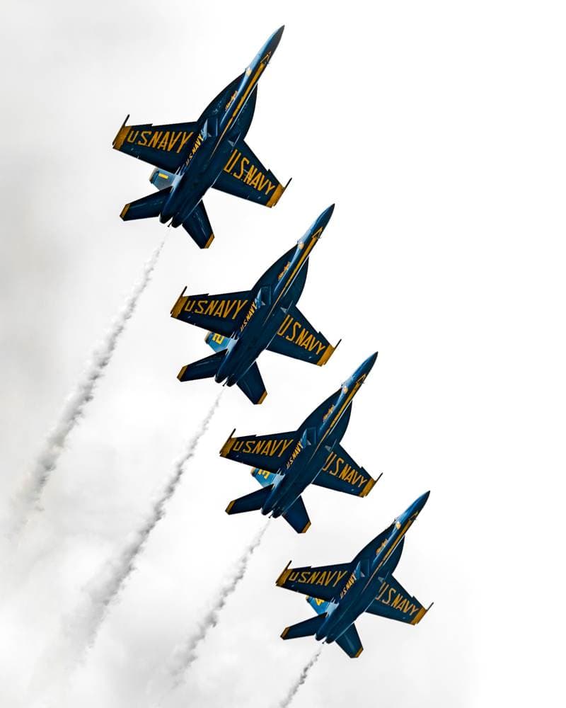 Four U.S. Navy Blue Angels jets flying in formation through a light sky