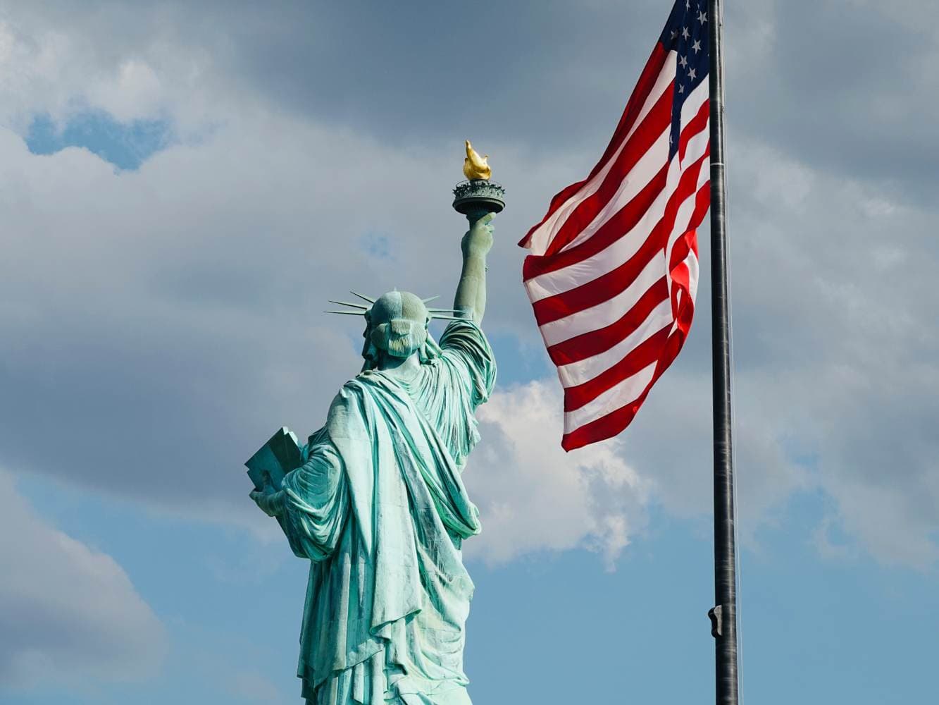 Statue of Liberty beside an American flag under a cloudy sky